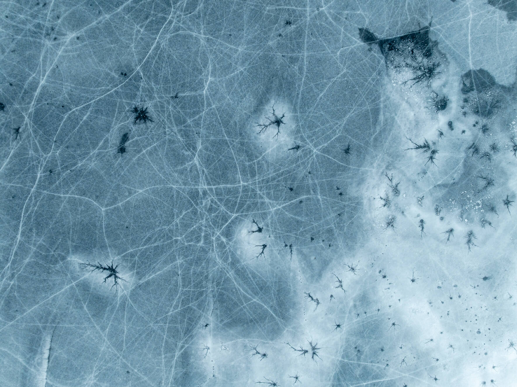 Aerial photograph of frozen lake surface with branching cracks in the ice