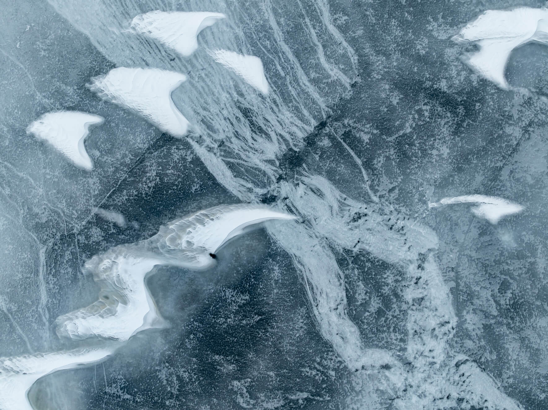 Aerial photograph of thawing ice surface with delicate snow ridges and pale blue tones