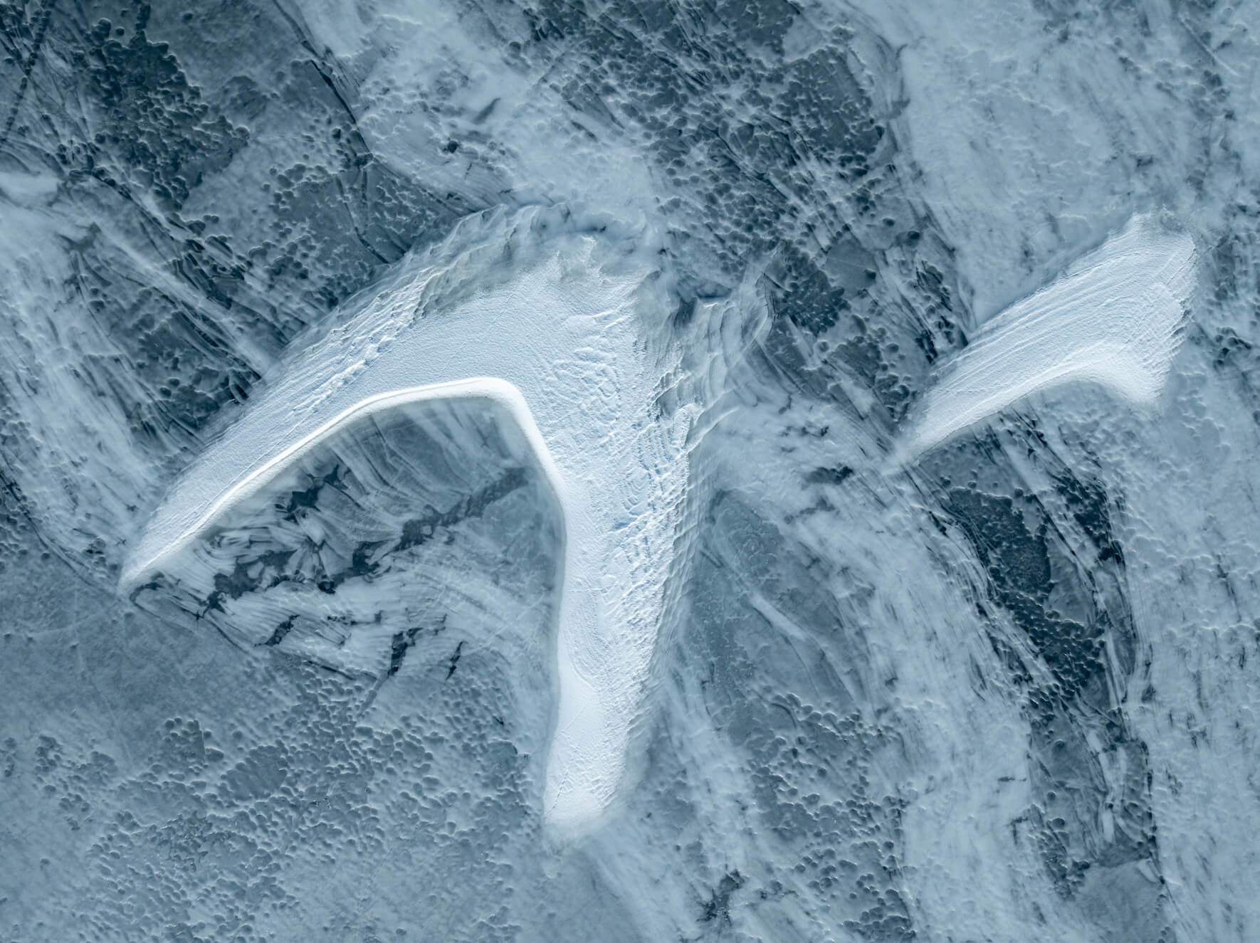 Aerial view of cracked frozen lake in Norway with snow drifts shaped like bird wings