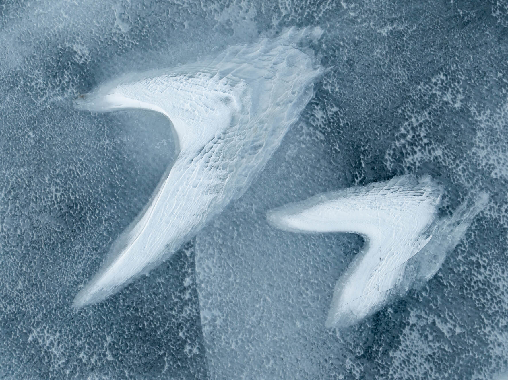 Frozen lake textures with sweeping snow curves resembling white wings on ice