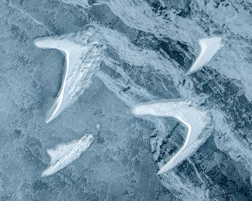 Frozen lake surface showing curved snow patterns shaped by wind and melting ice