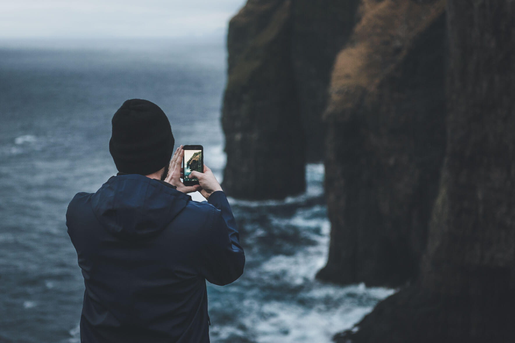 Man taking photo of Ásmundarstakkur sea stack on the Faroe Islands