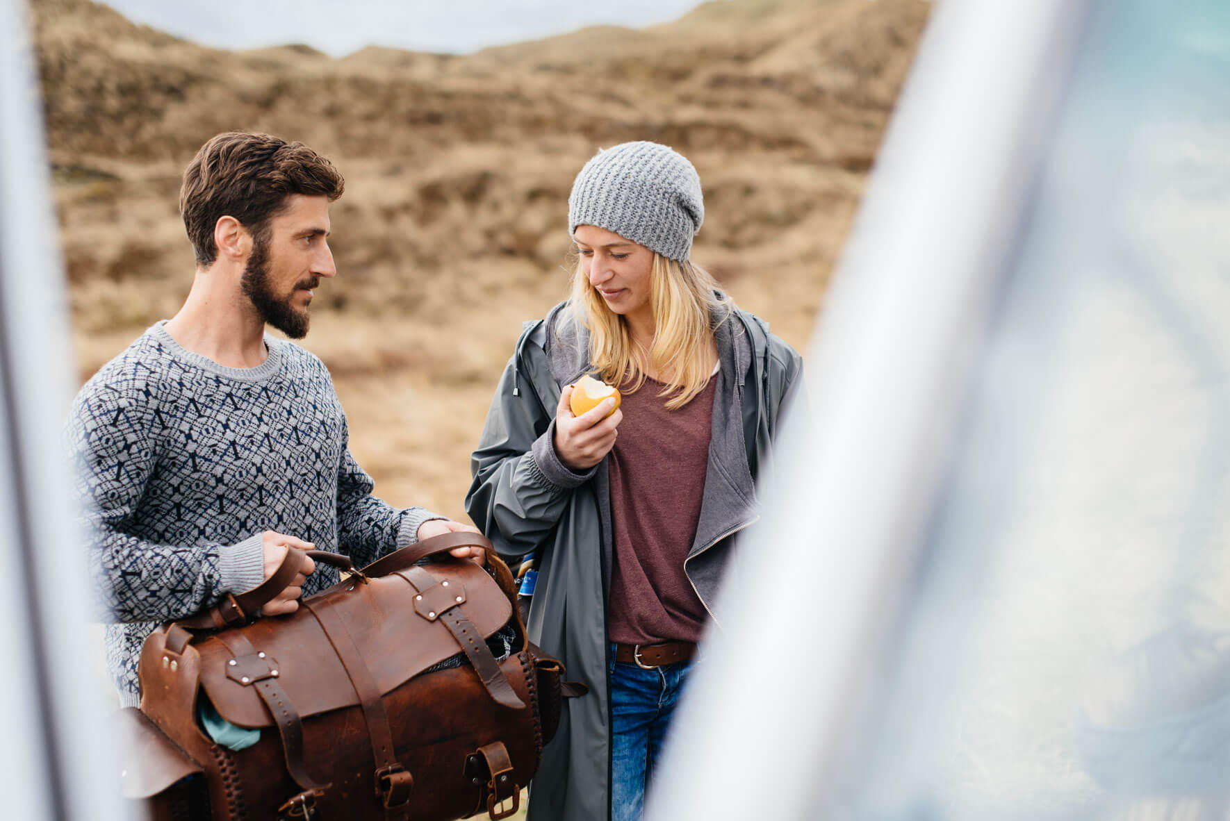 Two friends packing bag at camper van in the dunes